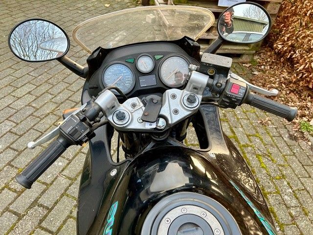 Auf einer gepflasterten Auffahrt ist ein schwarzes Motorrad geparkt.