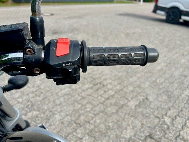 Nahaufnahme eines Motorrad-Gasgriffs mit rotem Schalter und schwarzem Griff im Freien