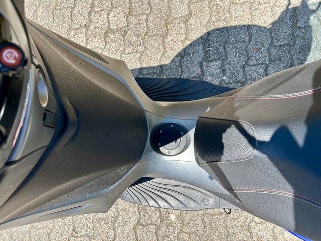 Ein Motorroller ist auf einem gepflasterten Gehweg geparkt und wirft einen Schatten auf den Boden.