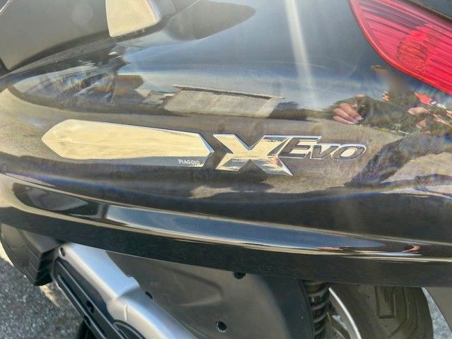 Nahaufnahme des Heckemblems eines Autos mit der Aufschrift „X Evo“ auf einer dunkelmetallicfarbenen Karosserie.