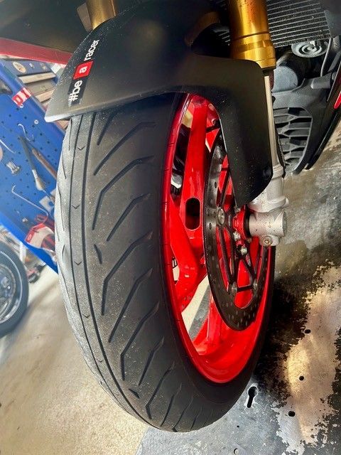 Nahaufnahme eines Motorradvorderrads mit roter Felge und schwarzem Reifen in einer Garage.