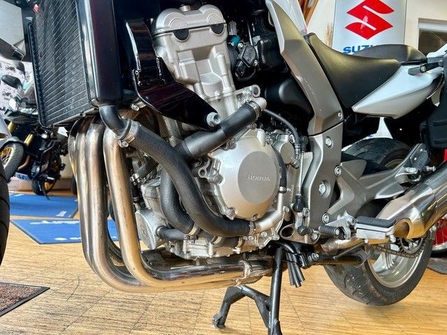 Nahaufnahme eines silbernen Suzuki-Motorradmotors mit Auspuffanlage, der in einem Ausstellungsraum steht.