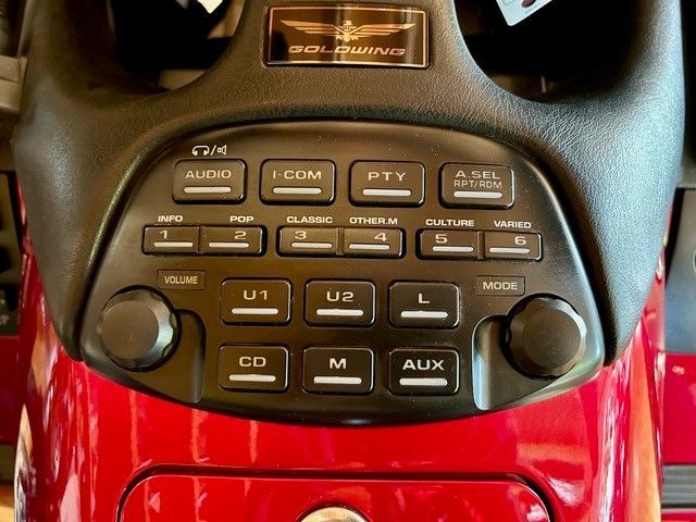 Nahaufnahme des roten Armaturenbretts eines Motorrads mit schwarzen Tasten für Audio-, Gegensprech- und Radiofunktionen.