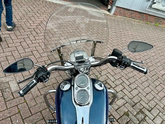 Eine Nahaufnahme des Lenkers, der Windschutzscheibe und der Anzeigen eines blauen Harley-Davidson-Motorrads, das auf einer gepflasterten Fläche geparkt ist.