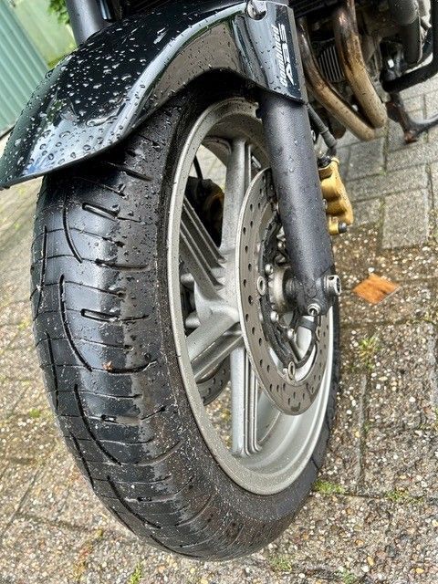 Nahaufnahme eines Motorradvorderrads und -reifens auf nasser Fahrbahn, schwarzer Schutzblech und Scheibenbremse sind sichtbar.