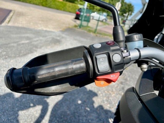 Motorradlenker mit Bedienelementen: schwarzer Griff, Handschutz, Blinker, Start-/Stoppschalter und Spiegel.
