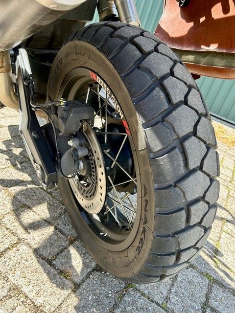 Nahaufnahme eines Motorradhinterrads mit Stollenreifen und Scheibenbremse auf Kopfsteinpflaster