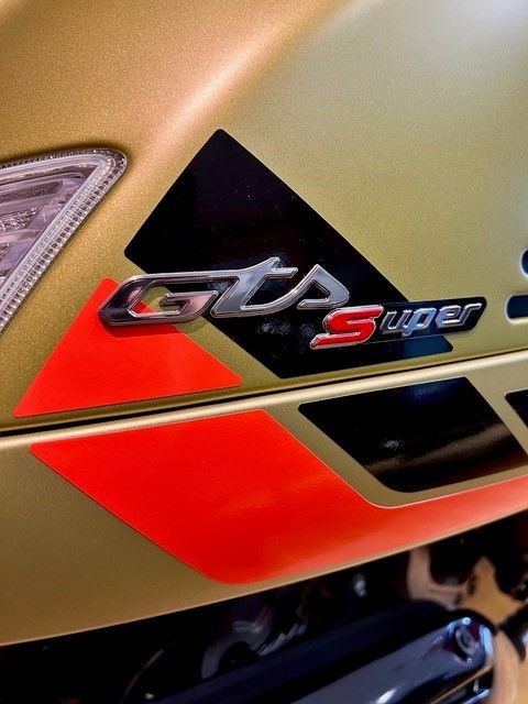 Goldenes Motorrad mit „GTS Super“-Emblem, roten und schwarzen Streifen.