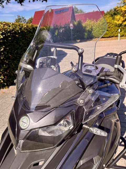Schwarzes Tourenmotorrad mit hoher Windschutzscheibe, das im Freien an einer sonnigen Straße parkt.