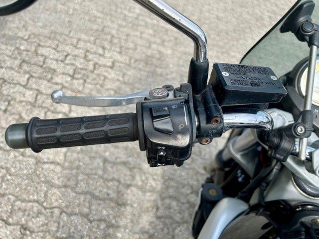 Nahaufnahme eines Motorradlenkers mit Gasgriff, Bremshebel und Bedienelementen auf einer asphaltierten Oberfläche