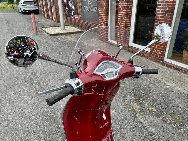 Ein roter Motorroller mit Windschutzscheibe ist vor einem Backsteingebäude geparkt.