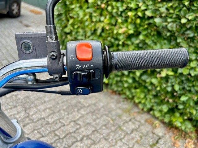 Motorradlenker mit schwarzen Bedienelementen, einem roten Schalter und einem grauen Griff.