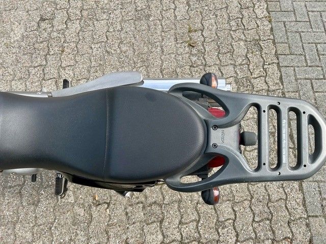 Draufsicht auf einen schwarzen Motorradsitz und einen silbernen Gepäckträger auf dem Asphalt
