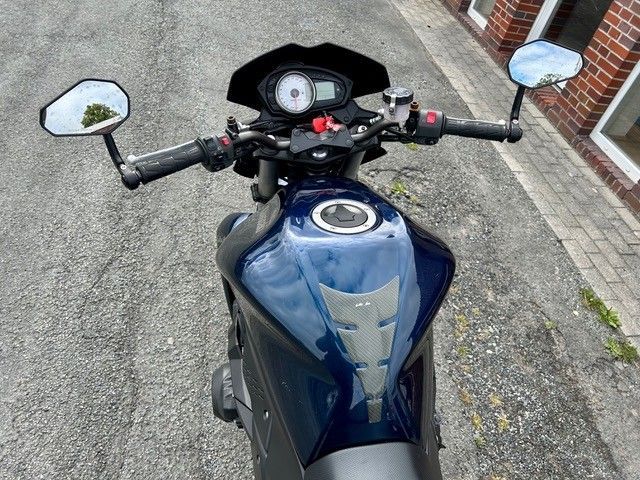 Blaues Motorrad, von oben auf einer asphaltierten Straße gesehen, Spiegel und Lenker sind sichtbar.