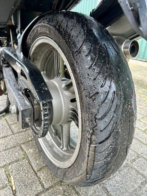 Nahaufnahme eines Motorradhinterreifens mit abgefahrenem Profil und nassem, schmutzigem Gummi in der Nähe der Radachse.