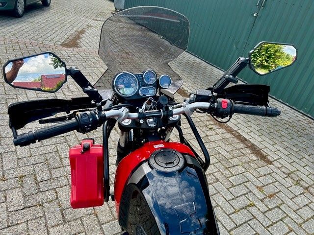 Ein rotes Motorrad parkt auf einer gepflasterten Auffahrt; von vorne gesehen, Spiegel und Instrumente sind sichtbar.