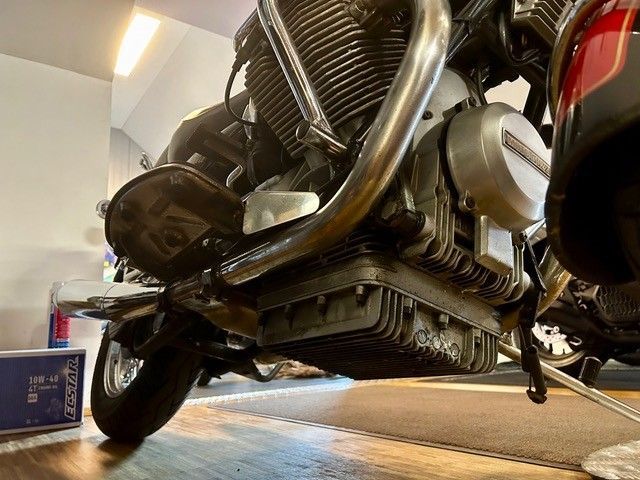 Ansicht von unten auf ein schwarzes Motorrad in einer Garage, die den Motor und die verchromten Auspuffrohre zeigt.
