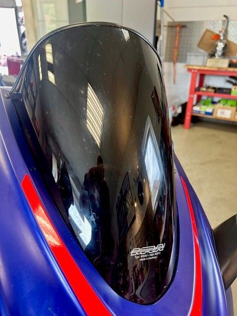 Nahaufnahme eines blauen Motorrads mit glänzend schwarzer Windschutzscheibe in einer Garage.