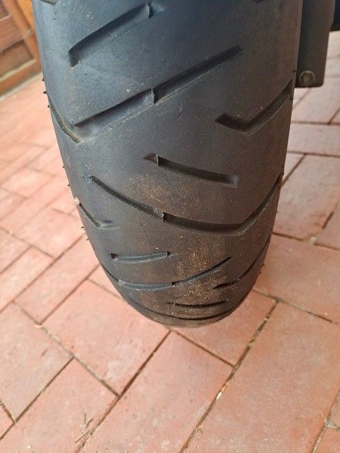 Nahaufnahme eines Motorradreifens mit abgenutztem Profil, der auf einem roten Backsteinpflaster liegt.