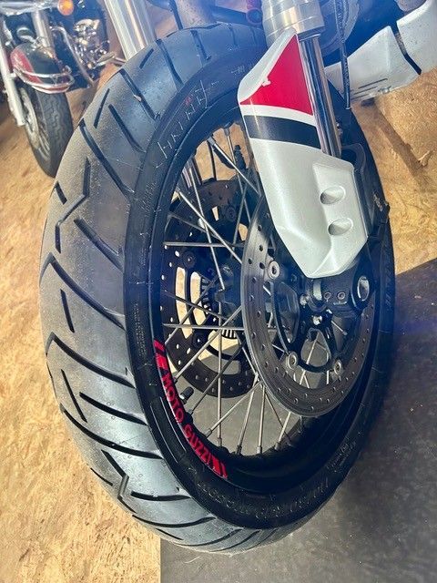 Nahaufnahme eines Motorradvorderrads mit schwarzem Reifen, roten Akzenten und silbernem Schutzblech in einer Garage.