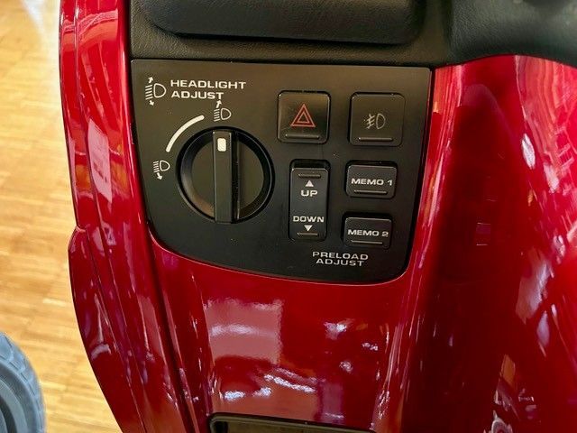 Rotes Motorrad-Bedienfeld mit Tasten für Scheinwerfer, Warnblinkanlage und Vorspannungseinstellung. Der Scheinwerferwinkel wird über ein Einstellrad eingestellt.