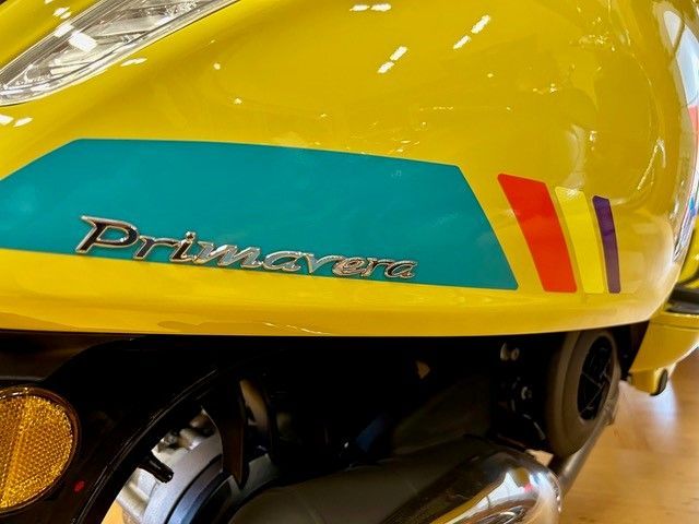 Gelbes Vespa Primavera-Rollerdetail mit blaugrünen und regenbogenfarbenen Akzentstreifen.