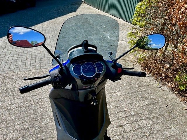 Ein Roller mit Windschutzscheibe ist auf einem gemauerten Bürgersteig geparkt