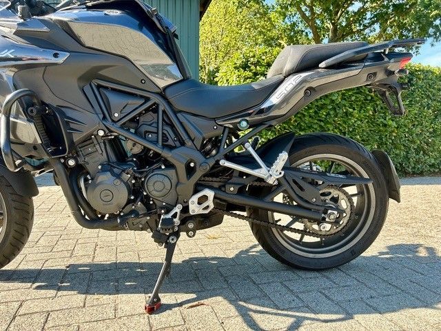 Silbernes und schwarzes Motorrad, geparkt auf einer gepflasterten Auffahrt neben Grünflächen, Seitenansicht auf dem Seitenständer.