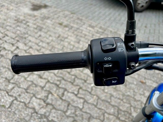 Schwarzer Motorradlenker mit Griff und Bedienschaltern, außen auf befestigter Fläche.