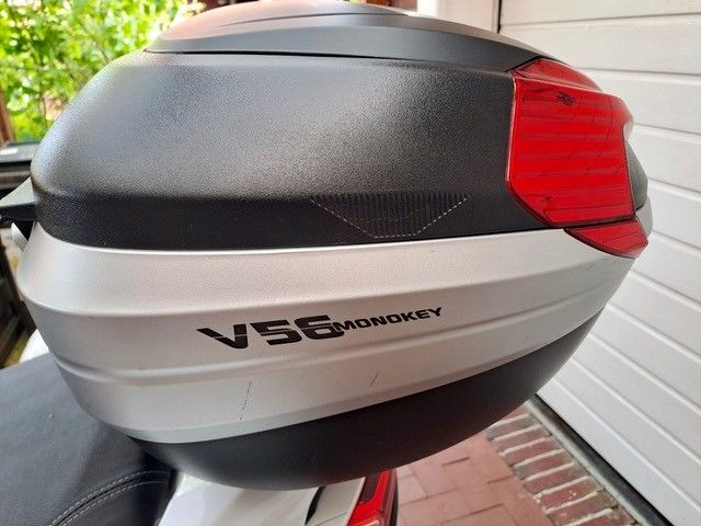 Ein schwarz-silbernes Motorrad-Topcase mit der Aufschrift „V56 MONOKEY“ und einem roten Rücklicht.