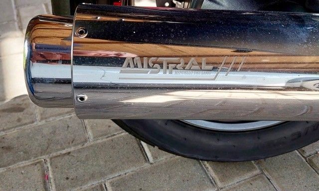 Glänzendes, verchromtes Mistral-Auspuffrohr an einem Motorrad, das auf einer Ziegeloberfläche ruht.