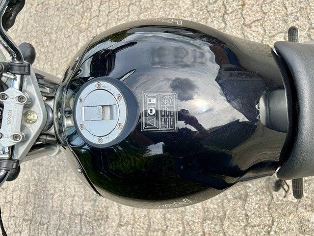 Draufsicht auf einen schwarzen Motorradtank mit silbernem Tankdeckel und sichtbarem Lenker.