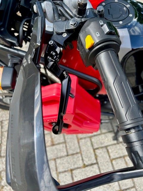 Nahaufnahme eines Motorradlenkers, Bremshebels und einer roten Verkleidung auf einer gepflasterten Oberfläche