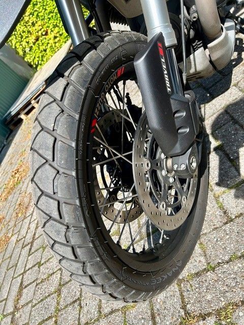 Nahaufnahme eines Motorradvorderrads mit Scheibenbremse und schwarzer Federung auf einer asphaltierten Straße