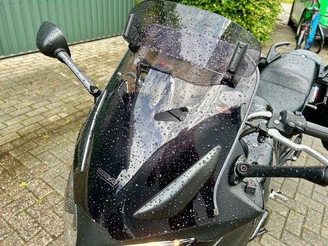 Schwarze Motorradscheibe und Spiegel, bedeckt mit Regentropfen, geparkt auf Ziegelpflaster.