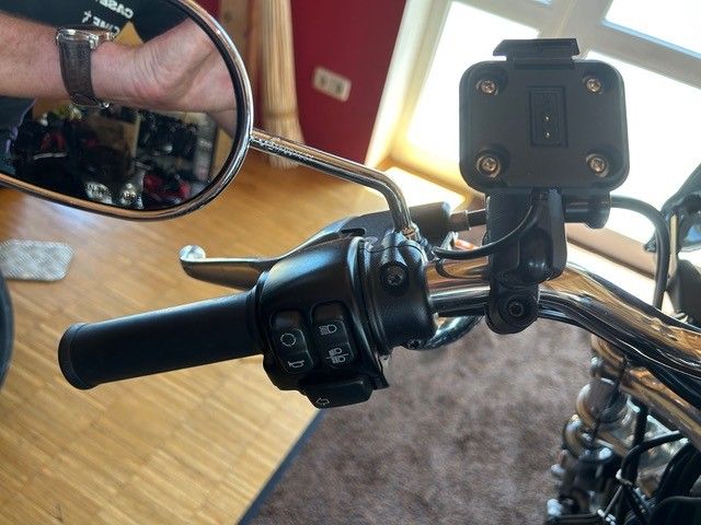 Fahrradlenker mit Schalthebel, Spiegel und montierter Action-Kamera in einer Werkstatt.