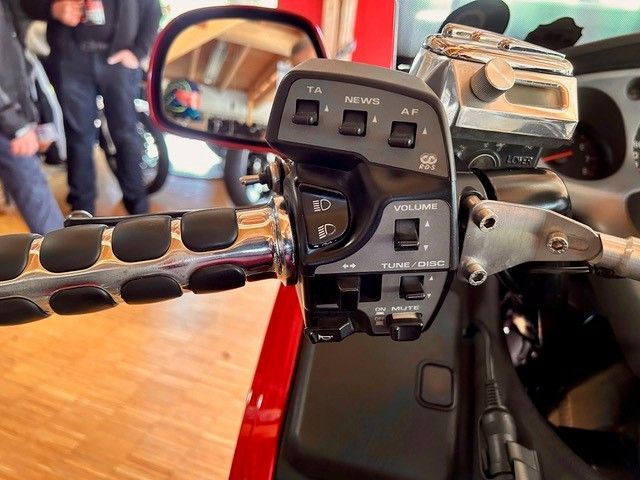 Nahaufnahme der Lenkersteuerung eines Motorrads, einschließlich Tasten für Radio, Licht und Lautstärke. Schwarzer Griff und rotes Gehäuse.