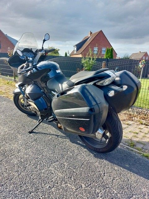 Schwarzes Tourenmotorrad mit Seitenkoffern, geparkt auf einer asphaltierten Auffahrt, bewölkter Himmel, Wohnhintergrund.