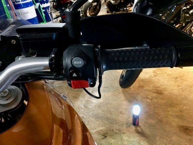 Eine Nahaufnahme des Lenkers eines Motorrads mit einer Taschenlampe im Hintergrund.