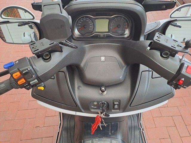 Armaturenbrettansicht eines schwarz-weißen Rollers mit Lenker, Spiegeln und Anzeigen. Der Schlüssel steckt im Zündschloss.