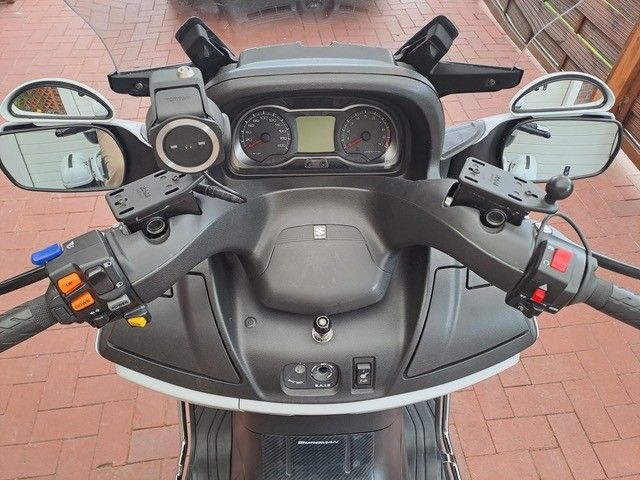 Draufsicht auf den Lenker und das Armaturenbrett eines Motorrollers mit mehreren Spiegeln, Steuertasten und einem kleinen Display.