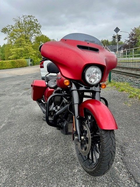 Rotes Tourenmotorrad, geparkt auf dem Bürgersteig, Vorderansicht, mit roter Verkleidung und Seitentaschen.