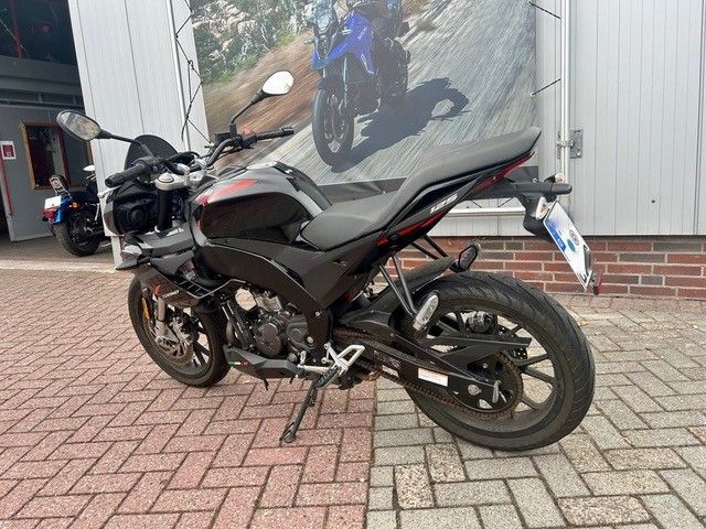 Ein schwarzes Sportmotorrad parkt auf einer gepflasterten Auffahrt neben einer Hauswand mit einem blauen Motorrad-Wandbild.
