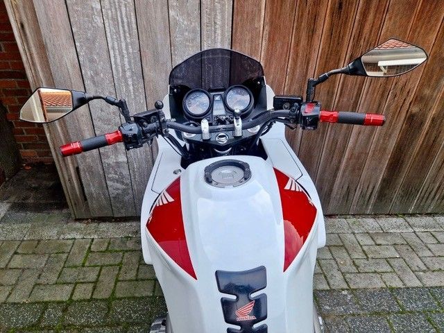 Draußen geparktes weiß-rotes Honda-Motorrad mit schwarzer Windschutzscheibe und roten Lenkergriffen.