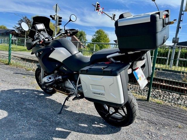 Ein schwarz-silbernes BMW-Motorrad mit daran befestigten Gepäckboxen, das neben einem Bahngleis geparkt ist.