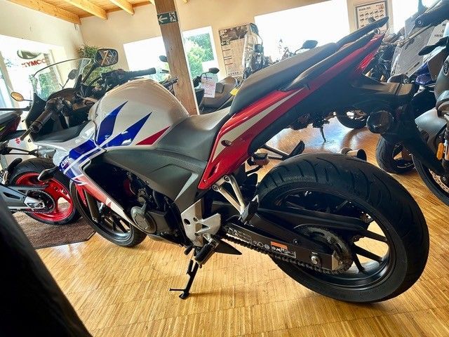 Ein rot-weiß-schwarzes Sportmotorrad steht in einer Garage oder einem Ausstellungsraum auf einem Bambusboden.