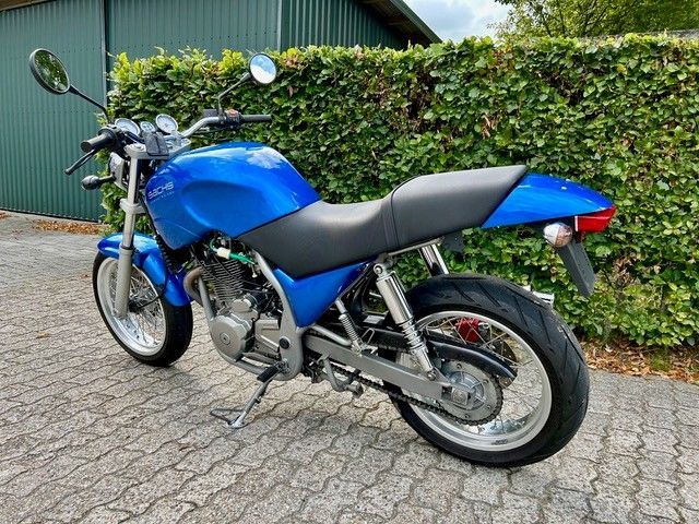 Blaues Motorrad, geparkt auf einer gepflasterten Auffahrt vor einer grünen Hecke.
