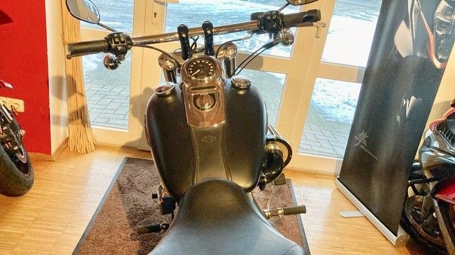 Ein schwarzes Motorrad steht auf einem Holzboden in einem Ausstellungsraum.
