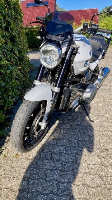 Weißes BMW-Motorrad auf dem Bürgersteig geparkt, Vorderansicht mit schwarzer Windschutzscheibe.