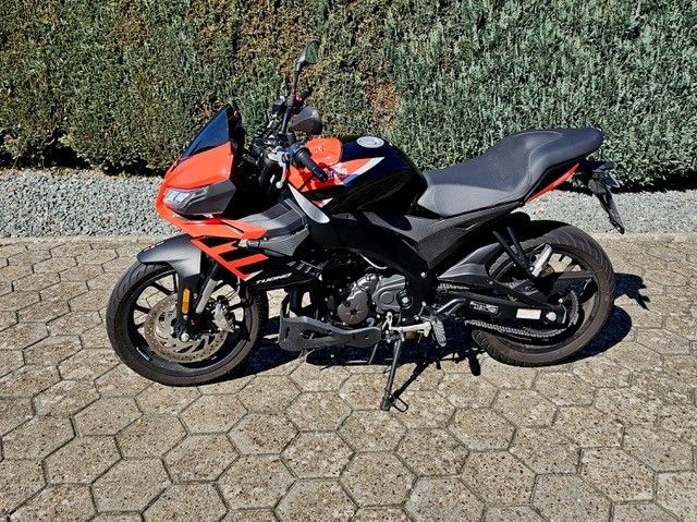Auf einer gepflasterten Auffahrt ist ein rot-schwarzes Motorrad geparkt.